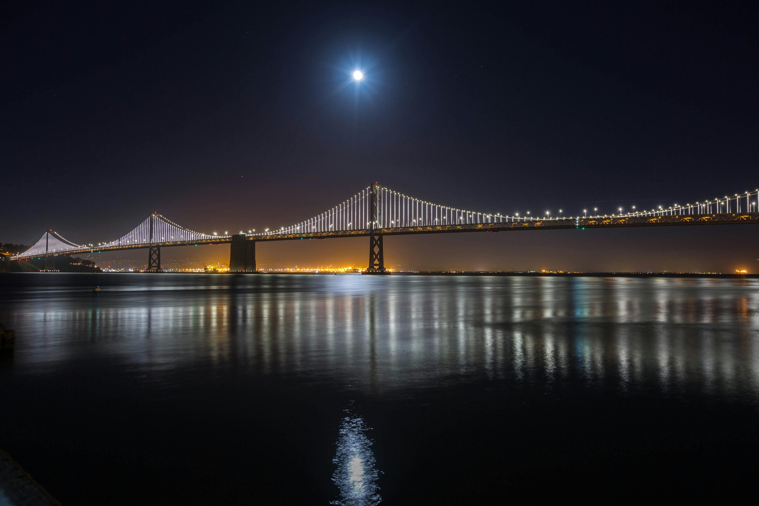 Stunning view of the illuminated Bay Bridge in San Francisco under moonlight reflection on water.